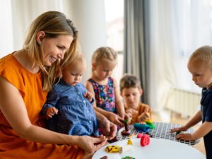 Mother or nursery teacher teaches her children to work with colorful play clay toys