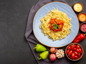 top view pasta on tablecloth plate of appetizing pasta next to the bowl of tomatoes and colorful