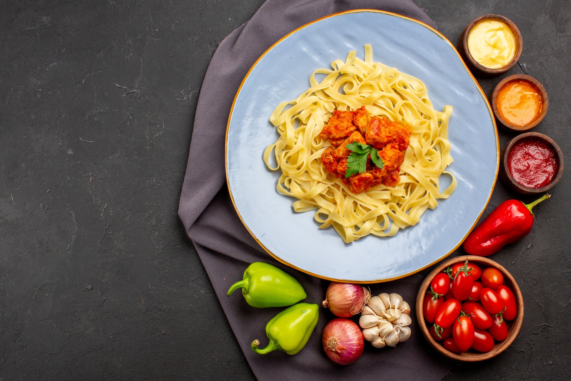 top view pasta on tablecloth plate of appetizing pasta next to the bowl of tomatoes and colorful