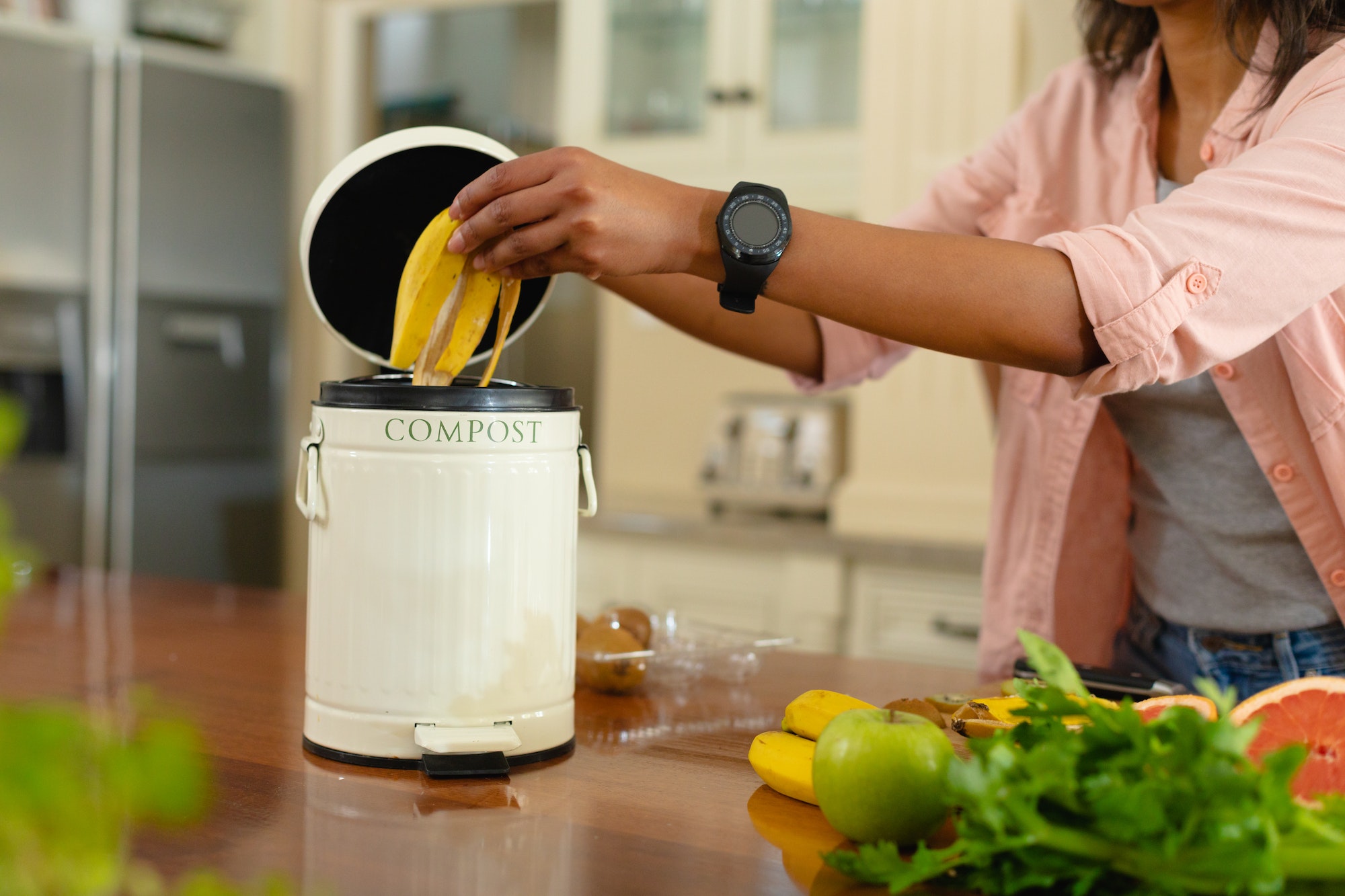 Midsection of young african american woman putting banana peel in compost bin at home