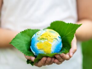 Kid holding small planet in hands against spring or summer green background. Ecology, environment