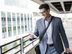 Happy businessman on business trip looking at his mini tablet
