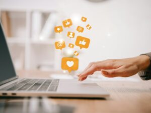 cropped view of businesswoman typing on laptop at workplace with multimedia icons
