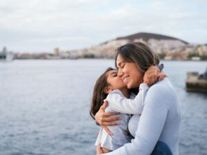 Mother and daughter embraced by the sea at sunset outdoors. Concept: Lifestyle, family care, love