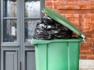Opened big green plastic trash can with full trash bags. Disposal of waste