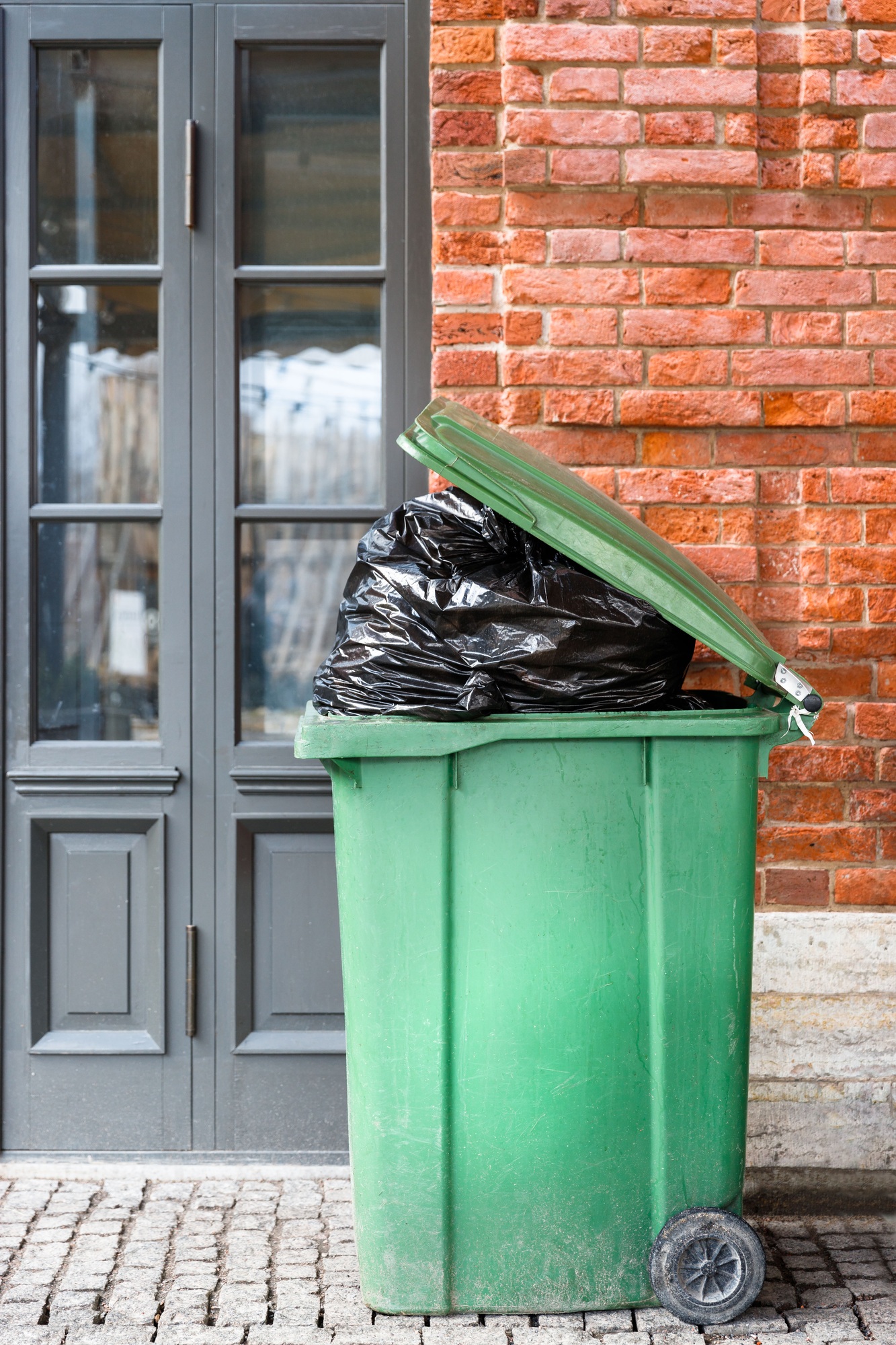 Opened big green plastic trash can with full trash bags. Disposal of waste